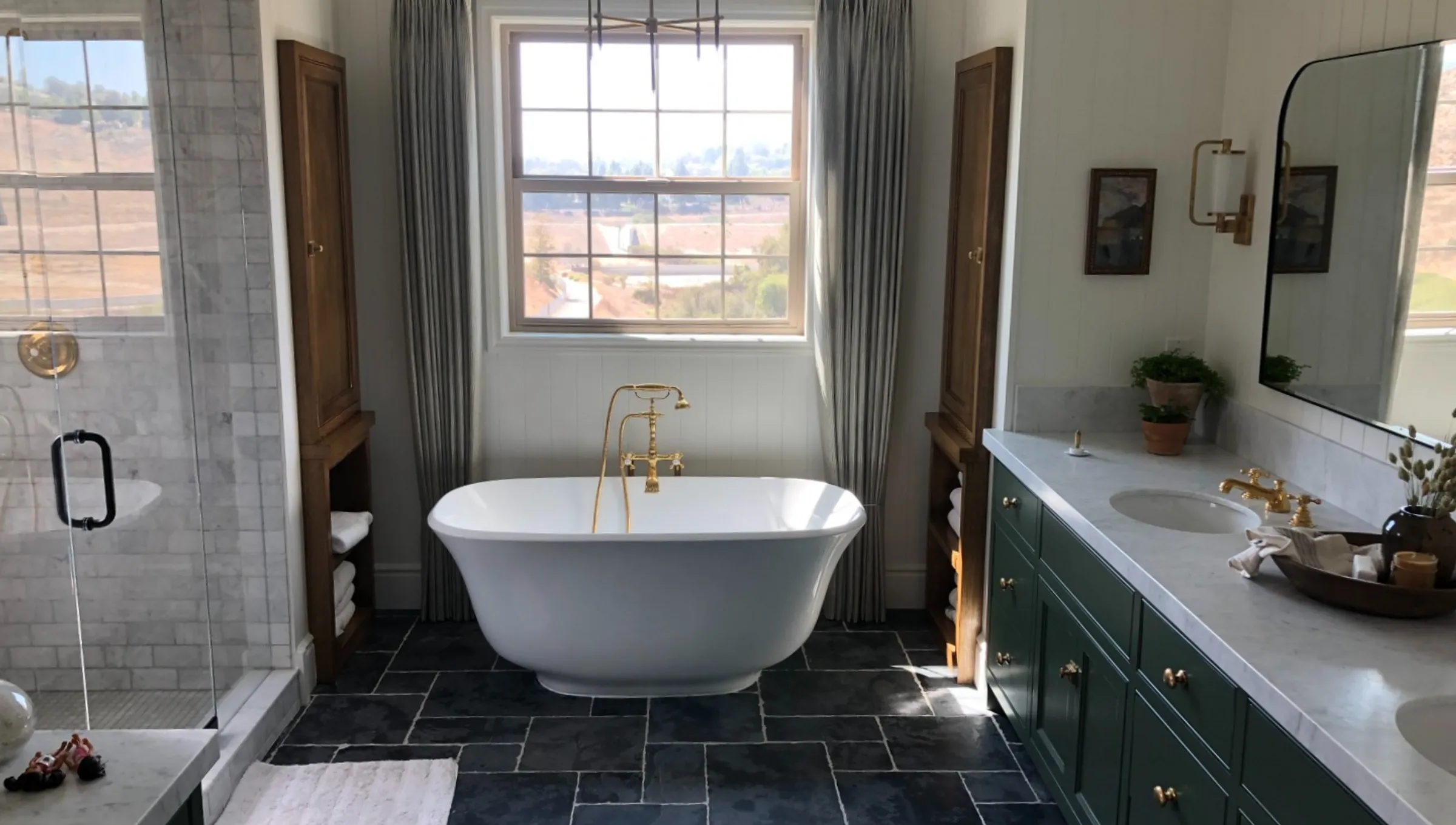 Freestanding soaking tub with an aged-brass floor-mounted filler in a marble-tiled bathroom