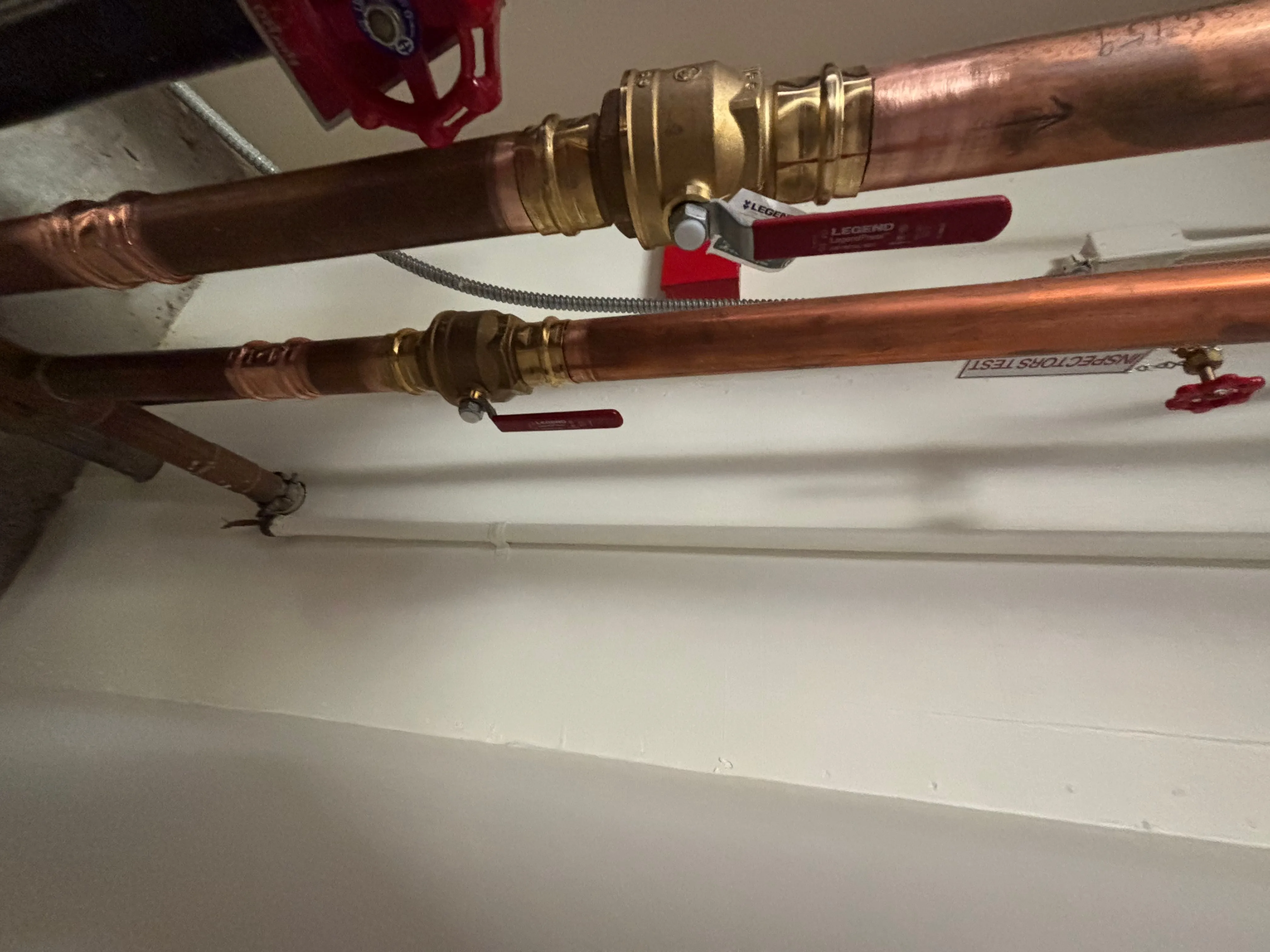 Vertical copper supply lines with brass ball valves and red handles on a commercial utility wall