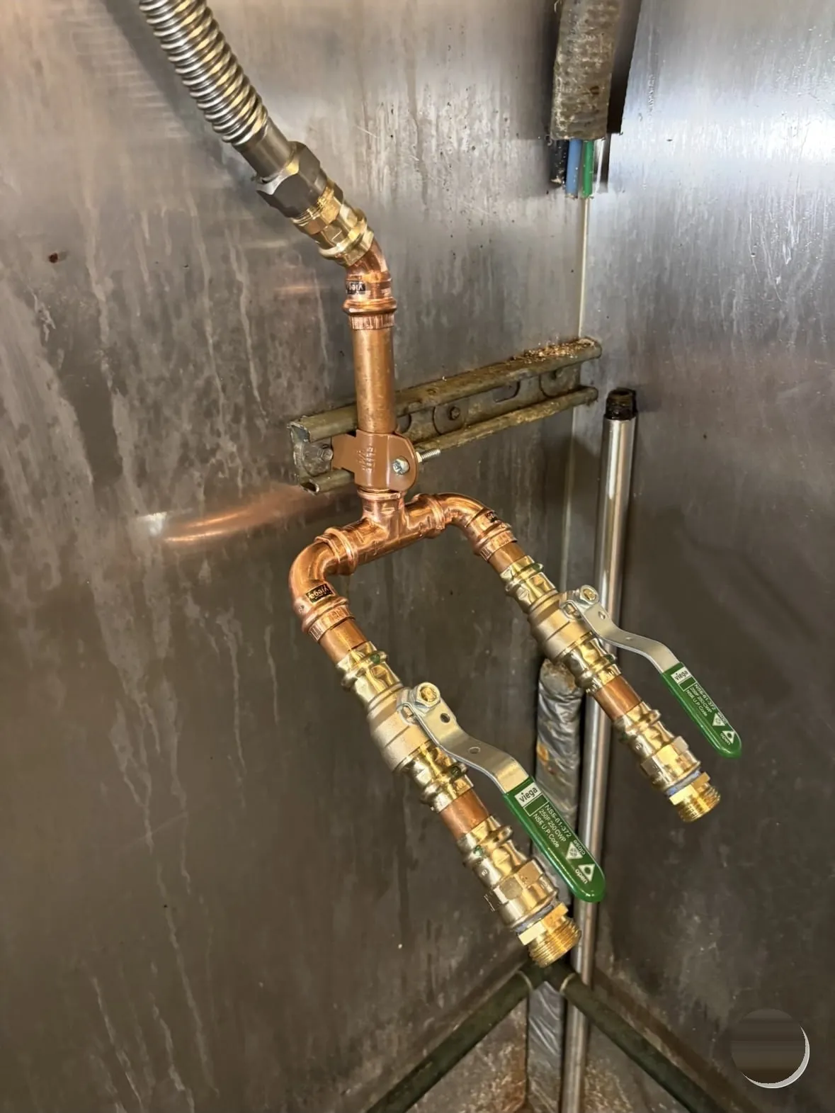 Copper manifold with green Viega ball valves on a stainless steel wall