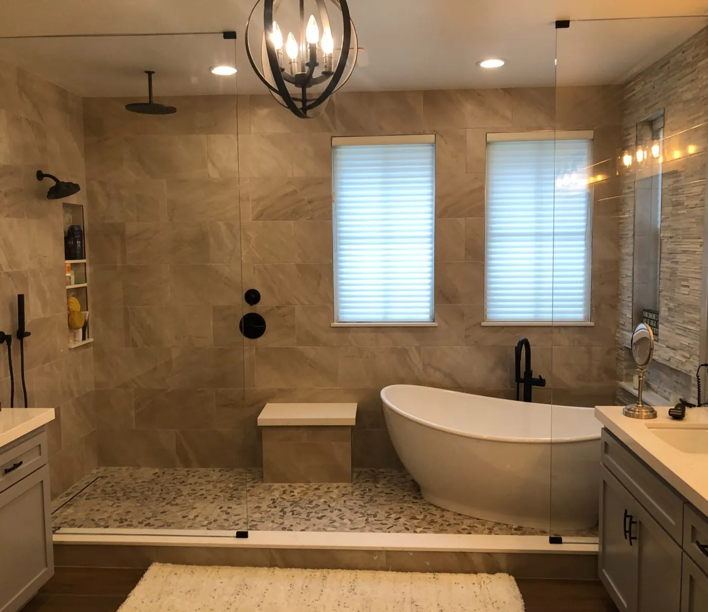 Stone-tiled bathroom with a pebble shower floor, freestanding tub and orb chandelier