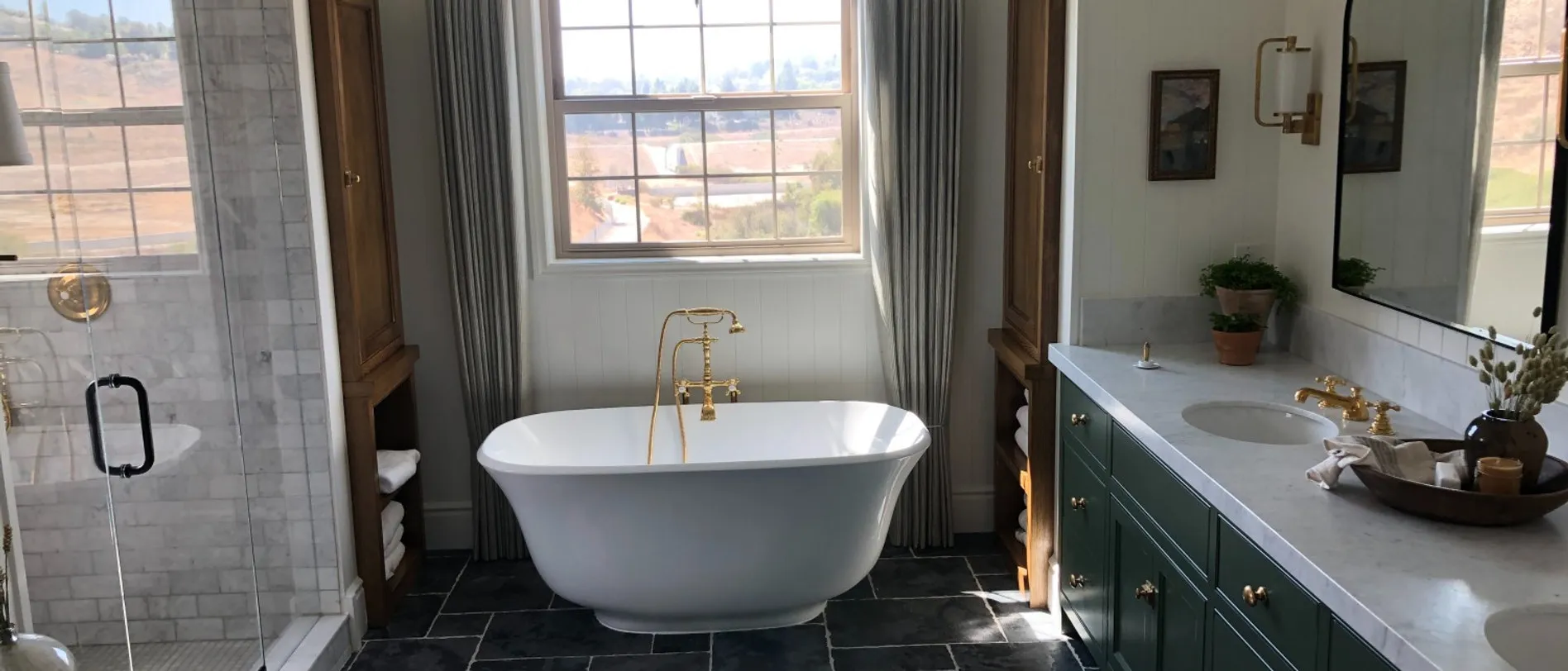 Primary bath with a freestanding tub, brass floor filler, green vanity and slate tile floor