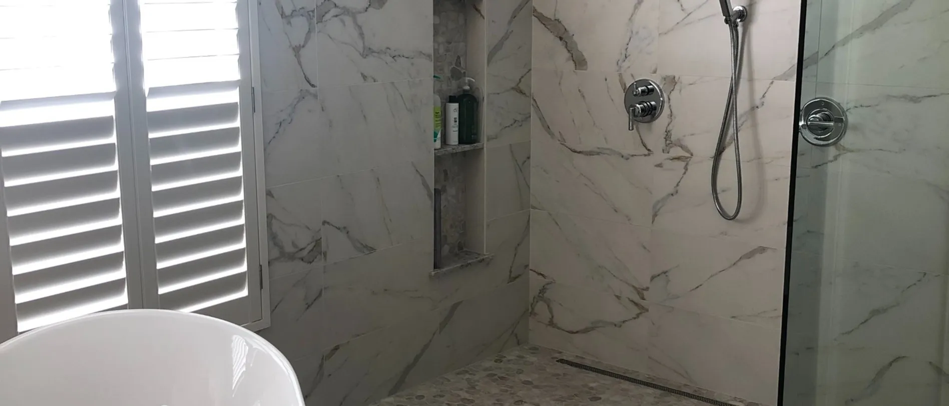 Curbless marble shower with chrome fixtures, a recessed niche and pebble floor