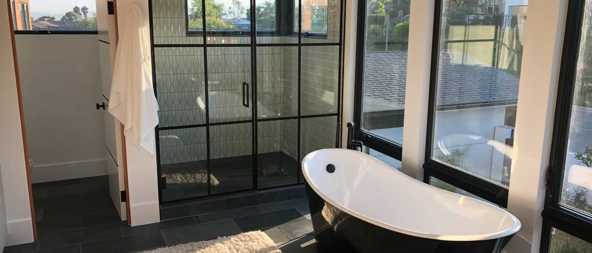 Black-framed glass shower enclosure and freestanding tub in a room with floor-to-ceiling windows